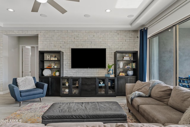 living room with light hardwood / wood-style flooring, ceiling fan, and brick wall