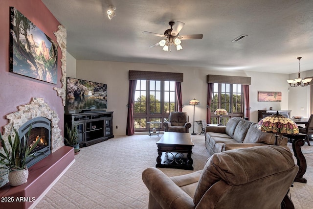 living area featuring visible vents, carpet floors, a stone fireplace, and ceiling fan with notable chandelier