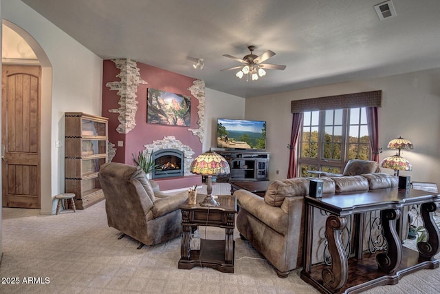 living room with visible vents, arched walkways, a fireplace, light colored carpet, and ceiling fan