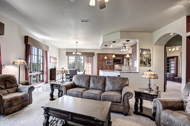 living area featuring visible vents, light carpet, ceiling fan with notable chandelier, a textured ceiling, and arched walkways