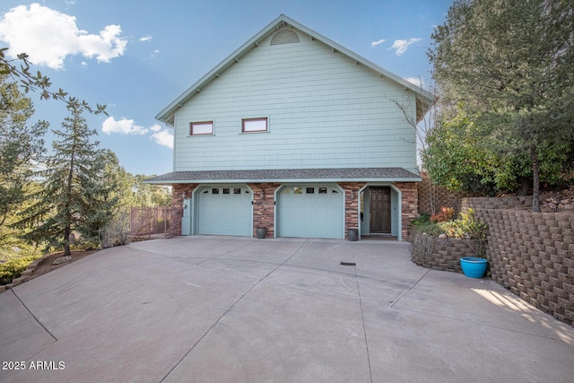 view of side of home featuring a garage, fence, stone siding, and driveway