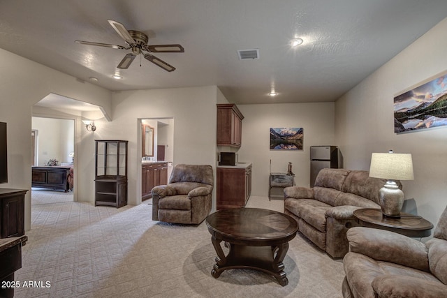 living area featuring visible vents, light carpet, arched walkways, and ceiling fan