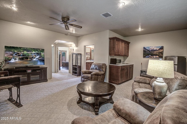 living area with visible vents, light carpet, a ceiling fan, a textured ceiling, and arched walkways