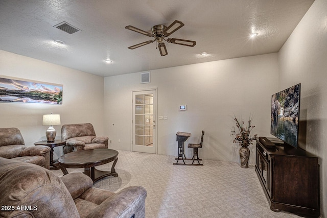 carpeted living area with a ceiling fan, visible vents, and a textured ceiling