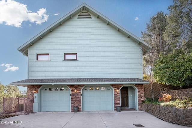 exterior space with a shingled roof, fence, concrete driveway, a garage, and stone siding