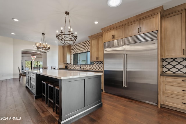 kitchen featuring a center island, light countertops, hanging light fixtures, dark wood-type flooring, and stainless steel built in refrigerator