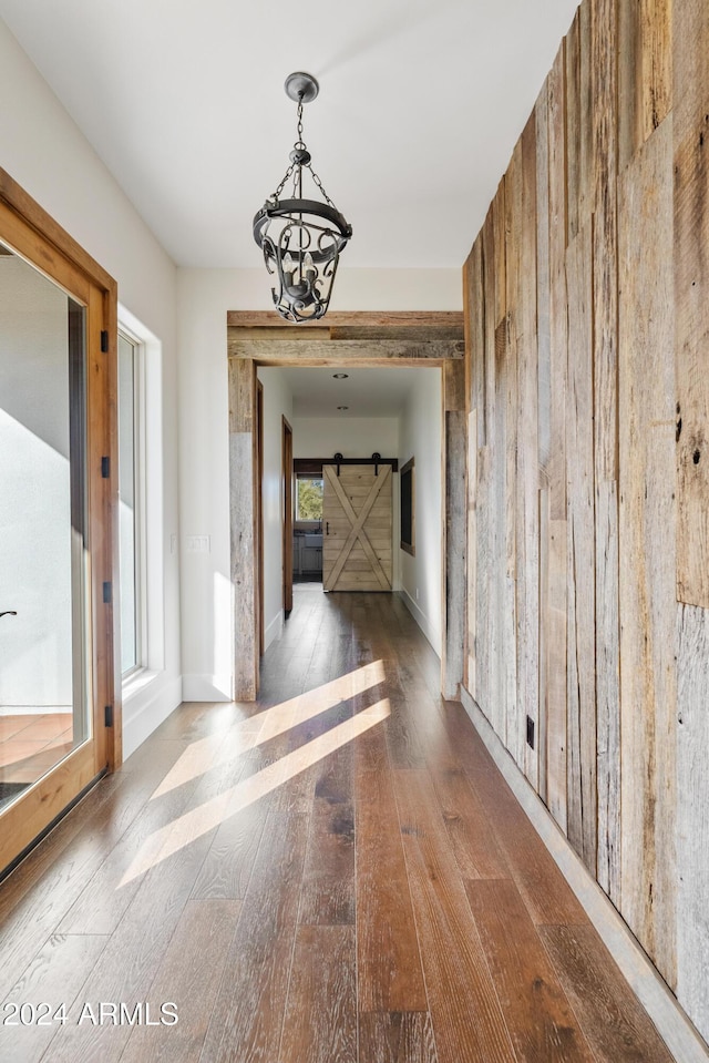 hall with wooden walls, a barn door, wood finished floors, and an inviting chandelier