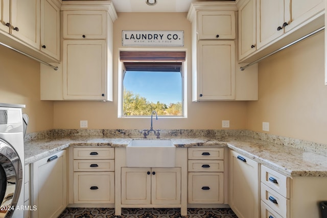 kitchen with cream cabinets, washer / clothes dryer, light stone counters, and a sink