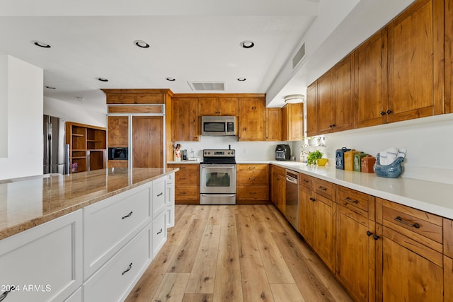 kitchen with light stone counters, visible vents, appliances with stainless steel finishes, brown cabinetry, and light wood-type flooring