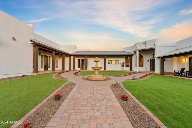 back of property at dusk featuring metal roof, a yard, a standing seam roof, and stucco siding