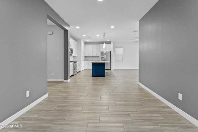 kitchen with white cabinetry, hanging light fixtures, a center island with sink, a kitchen breakfast bar, and stainless steel appliances