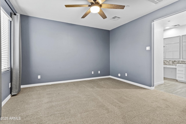 unfurnished bedroom featuring ensuite bathroom, built in desk, light colored carpet, and ceiling fan