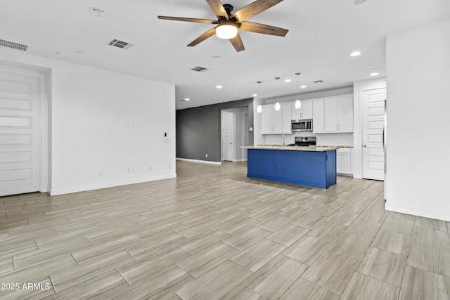 kitchen featuring decorative light fixtures, white cabinetry, a kitchen island with sink, light stone counters, and stainless steel appliances