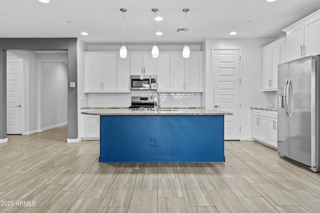 kitchen with white cabinetry, hanging light fixtures, stainless steel appliances, light stone countertops, and a kitchen island with sink