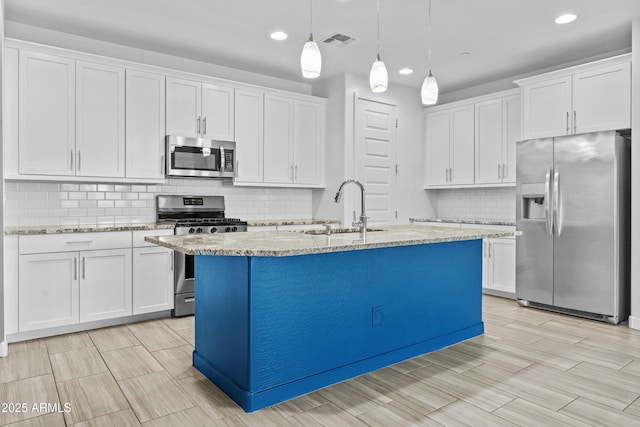 kitchen featuring sink, appliances with stainless steel finishes, white cabinetry, a kitchen island with sink, and hanging light fixtures