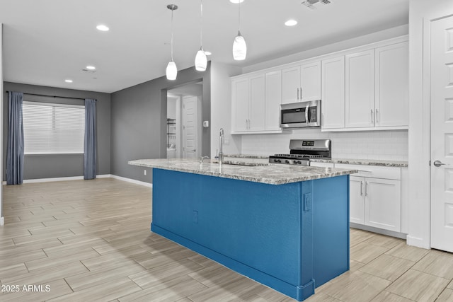 kitchen featuring sink, white cabinetry, decorative light fixtures, appliances with stainless steel finishes, and an island with sink