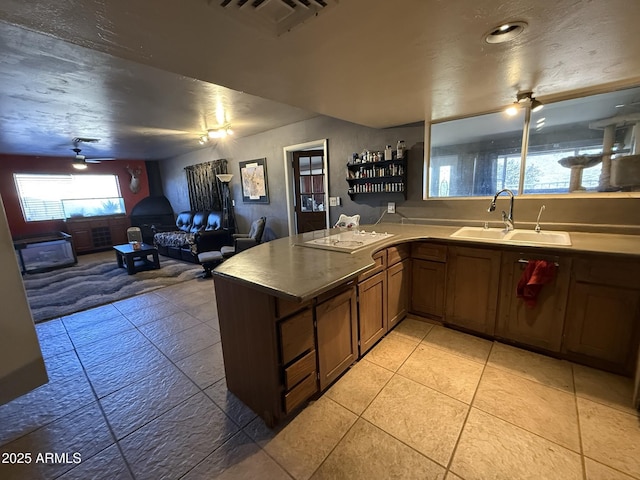 kitchen with kitchen peninsula, ceiling fan, a wood stove, white stovetop, and sink