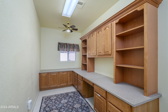 unfurnished office featuring ceiling fan, built in desk, and light tile patterned floors