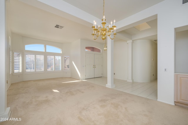 spare room featuring a chandelier, light colored carpet, and decorative columns