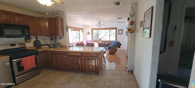 kitchen featuring stainless steel gas range oven, ceiling fan, kitchen peninsula, and light tile patterned flooring