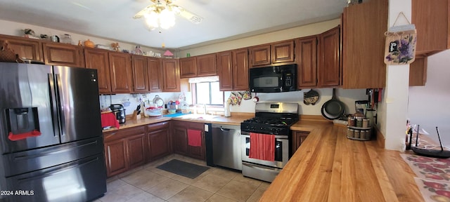 kitchen with ceiling fan, sink, wood counters, light tile patterned floors, and appliances with stainless steel finishes