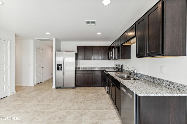 kitchen featuring sink, light tile patterned floors, dark brown cabinets, stainless steel appliances, and light stone countertops