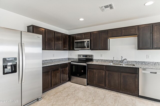 kitchen with light stone counters, dark brown cabinetry, stainless steel appliances, and sink