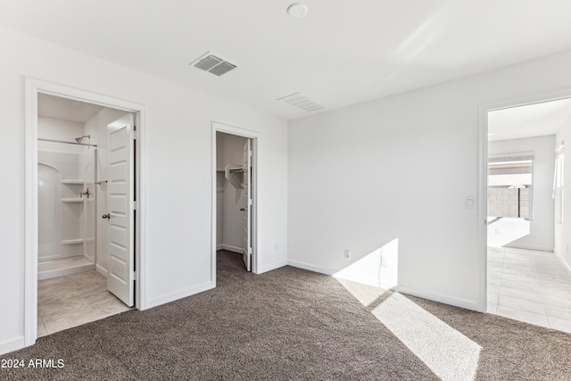 unfurnished bedroom with light carpet, a spacious closet, a closet, and ensuite bathroom