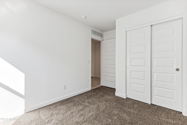 unfurnished bedroom with dark colored carpet and a closet