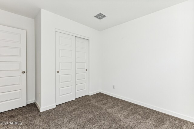 unfurnished bedroom featuring dark carpet and a closet