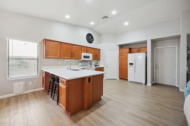 kitchen featuring sink, white appliances, light hardwood / wood-style flooring, a breakfast bar, and kitchen peninsula