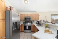 kitchen with kitchen peninsula, sink, light tile patterned flooring, and appliances with stainless steel finishes