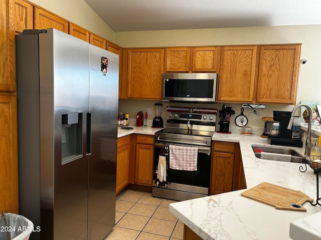 kitchen with sink, light tile patterned floors, vaulted ceiling, and appliances with stainless steel finishes