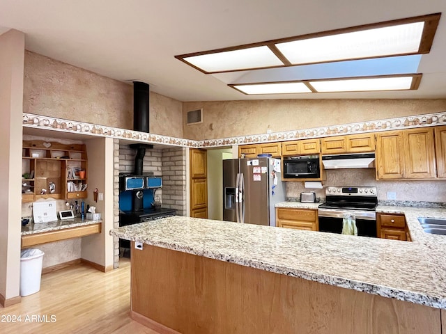 kitchen with appliances with stainless steel finishes, kitchen peninsula, light hardwood / wood-style floors, lofted ceiling, and light stone counters