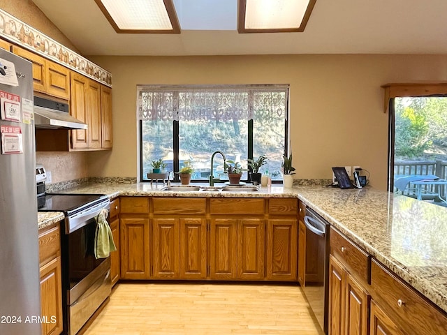 kitchen with light stone counters, appliances with stainless steel finishes, sink, and light wood-type flooring