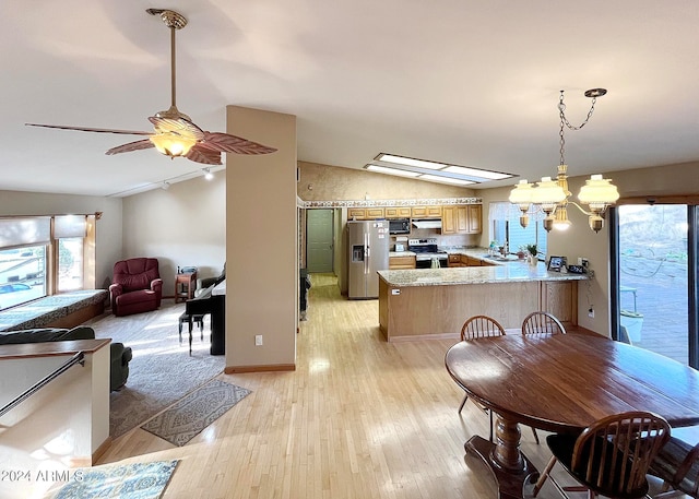 kitchen featuring kitchen peninsula, stainless steel appliances, vaulted ceiling with skylight, light wood-type flooring, and ceiling fan with notable chandelier