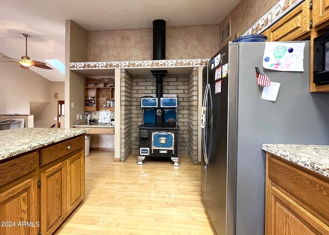 kitchen featuring ceiling fan, light wood-type flooring, light stone counters, stainless steel refrigerator, and a skylight