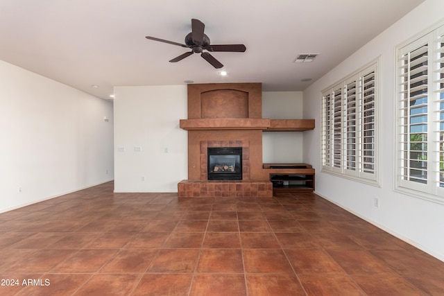 unfurnished living room with ceiling fan, dark tile patterned flooring, a fireplace, visible vents, and baseboards