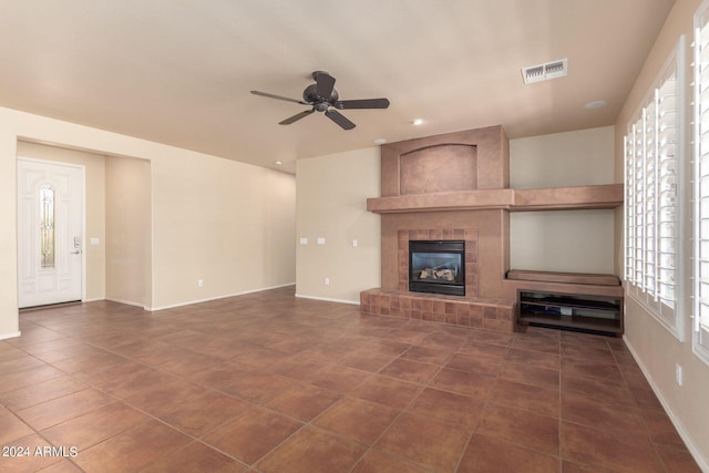 unfurnished living room with a fireplace, ceiling fan, and dark tile patterned floors