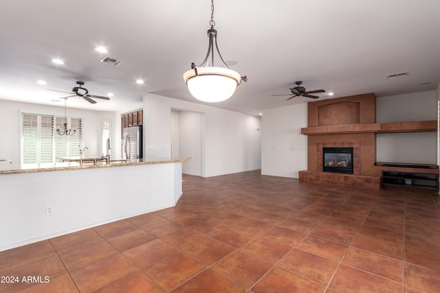 unfurnished living room with ceiling fan with notable chandelier, a fireplace, and visible vents