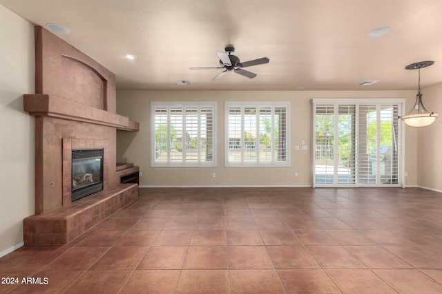 unfurnished living room with ceiling fan, a tiled fireplace, and tile patterned floors