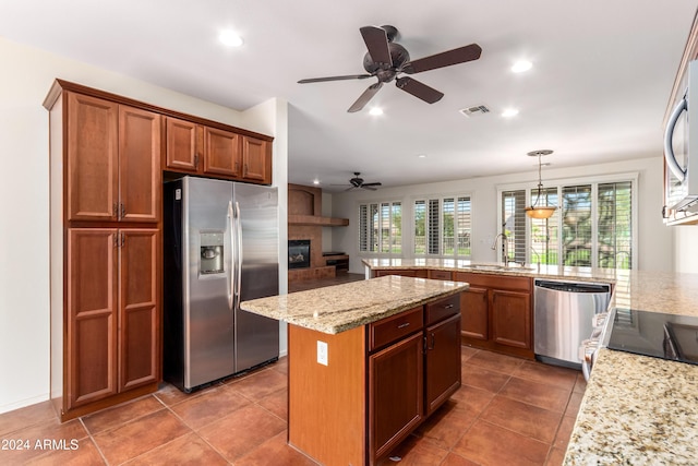 kitchen with light stone counters, stainless steel appliances, a sink, brown cabinets, and decorative light fixtures