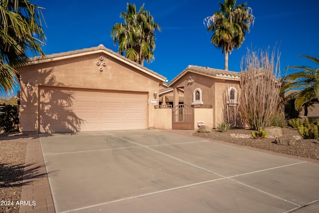 mediterranean / spanish house featuring stucco siding, a gate, a garage, driveway, and a tiled roof