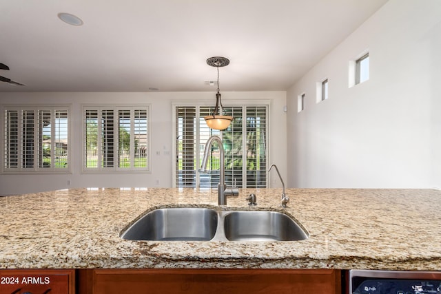 kitchen featuring light stone counters, a sink, decorative light fixtures, and a healthy amount of sunlight