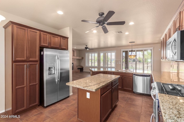 kitchen with appliances with stainless steel finishes, dark tile patterned flooring, light stone counters, a kitchen island, and ceiling fan