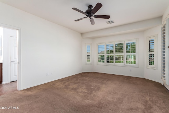 unfurnished room with dark colored carpet, visible vents, ceiling fan, and baseboards