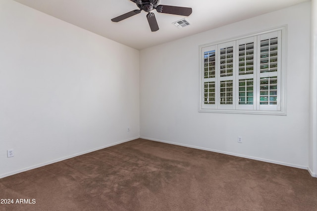 unfurnished room with a ceiling fan, visible vents, dark carpet, and baseboards