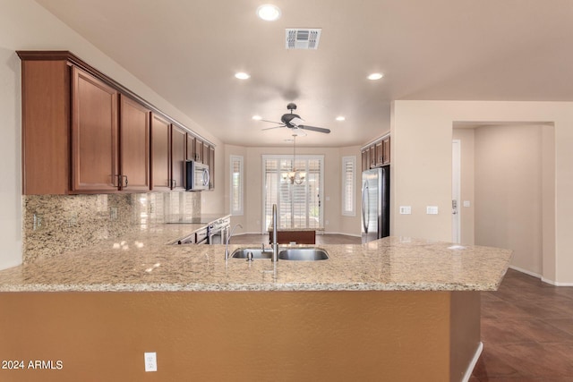 kitchen with ceiling fan with notable chandelier, appliances with stainless steel finishes, light stone countertops, sink, and dark tile patterned flooring