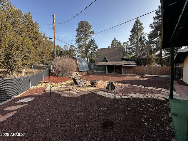 view of yard featuring an outdoor structure, a fenced backyard, and a fire pit