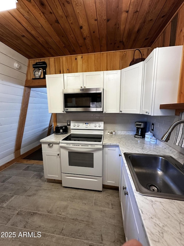 kitchen with white cabinets, wood walls, stainless steel microwave, a sink, and white range with electric cooktop